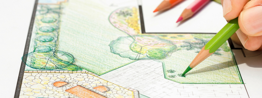 Closeup of a person using colored pencils and paper to draw a garden plan