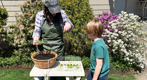 An adult Ferry-Morse gardener showing a young gardener how they're going to put together a statement hanging basket.